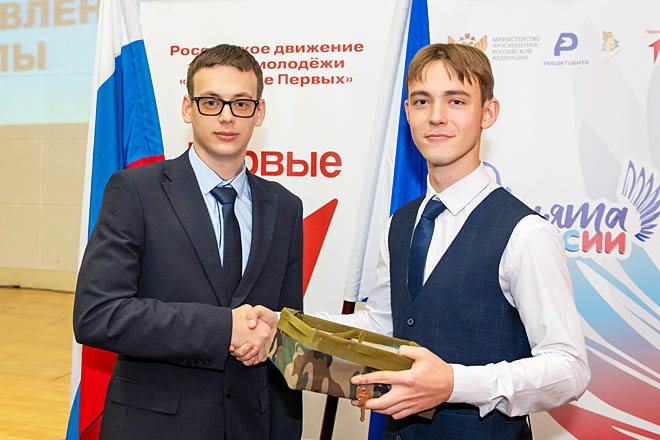 Экс-президент школы Артур Селезнёв (слева) во время символической передачи «Эстафеты проектов» вручил своему преемнику ключи от почтового ящика обращений участников школьного сообщества, а также коробку с лентами для плетения маскировочных сетей для бойцов СВО.